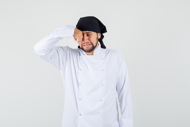 Male chef rubbing eye while crying like a child in white uniform and looking offended. front view.