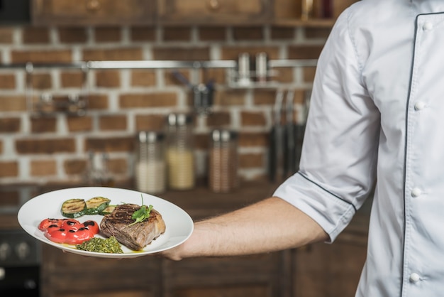 Free photo male chef's hand holding delicious beef steak dish with roasted veggies