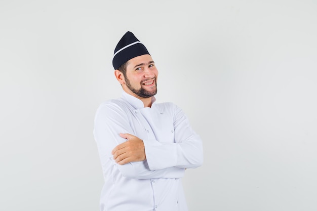 Male chef standing with crossed arms in white uniform and looking merry , front view.