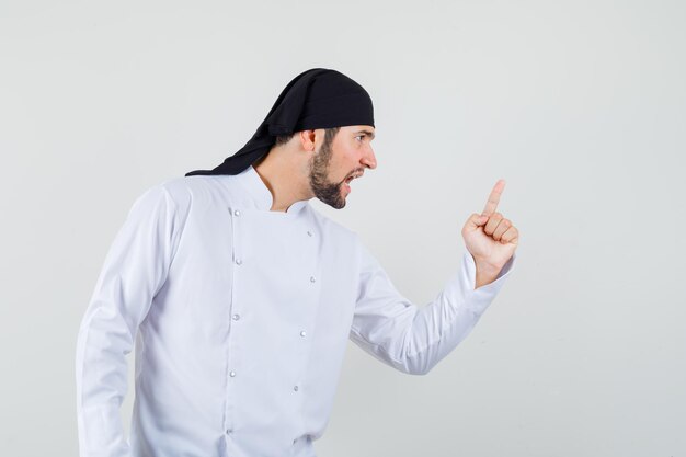 Male chef warning somebody with finger in white uniform and looking nervous. front view.