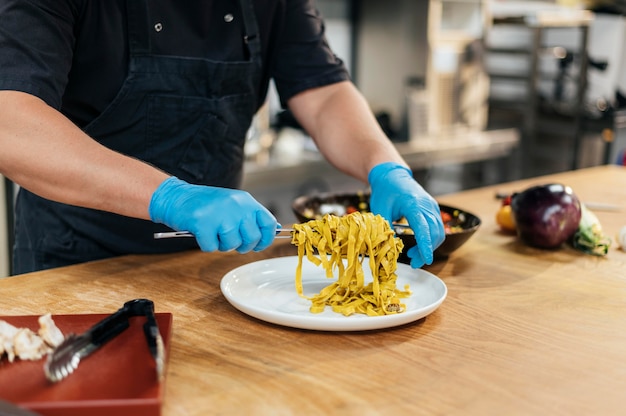 Free photo male chef with gloves putting pasta on plate