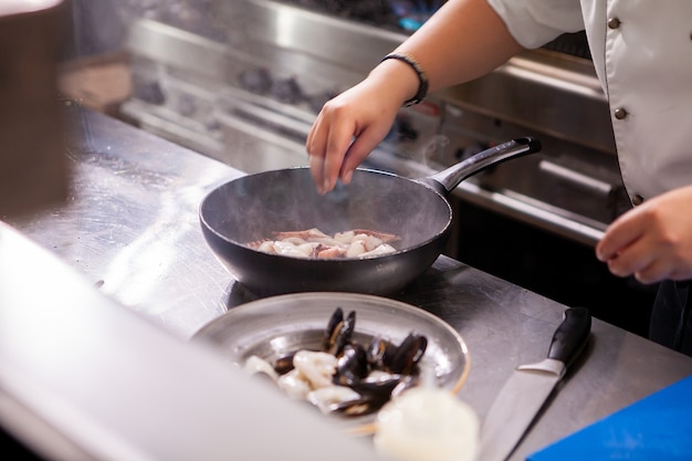 Male cook fries seafood at stove in kitchen restaurant