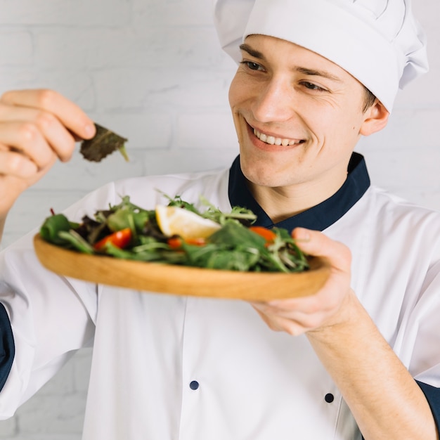 Male cook looking at wooden plate with salad