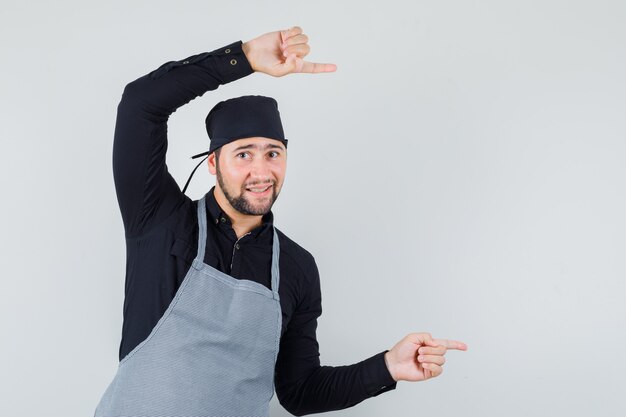 Male cook pointing to the side and smiling in shirt, apron , front view.