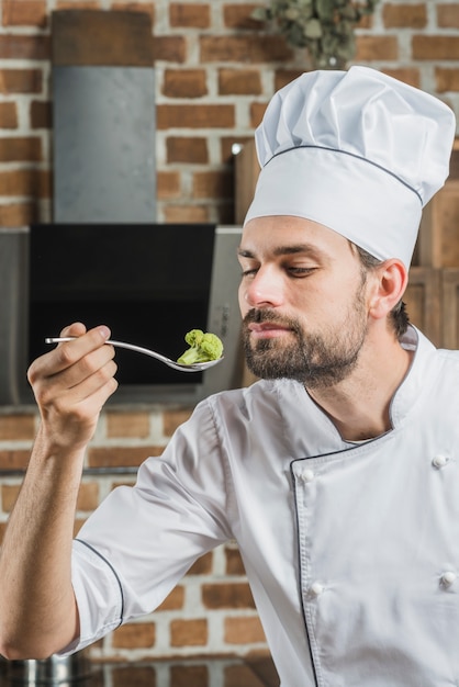 Male cook smelling green broccoli in spoon