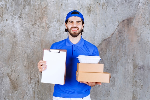 Free photo male courier in blue uniform carrying cardboard and plastic boxes and presenting the signature list