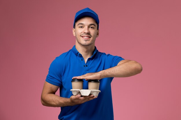 male courier in blue uniform delivering coffee cups on pink, worker uniform service delivery