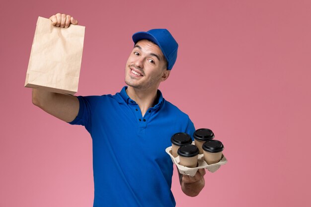 male courier in blue uniform holding delivery coffee cups food package on pink, uniform job service delivery