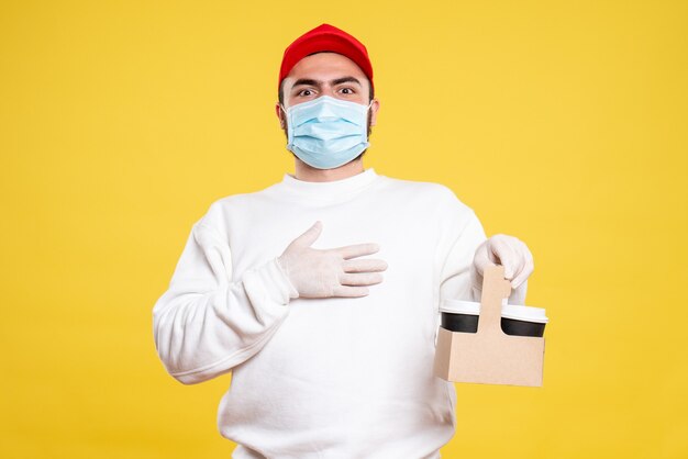 male courier in mask holding delivery coffee on light yellow