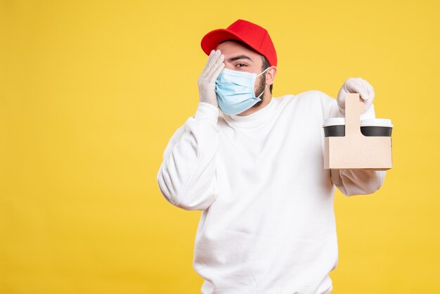 male courier in mask holding delivery coffee on yellow