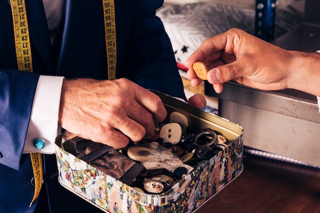 Male customer selecting button from the container hold by fashion designer