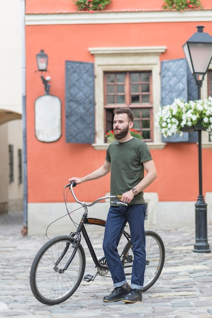 Free photo male cyclist standing with his bicycle in front of building