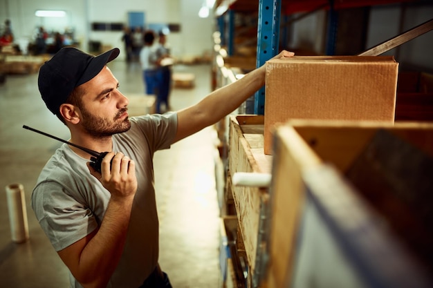 Male dispatcher checking packages while using walkietalkie in distribution warehouse