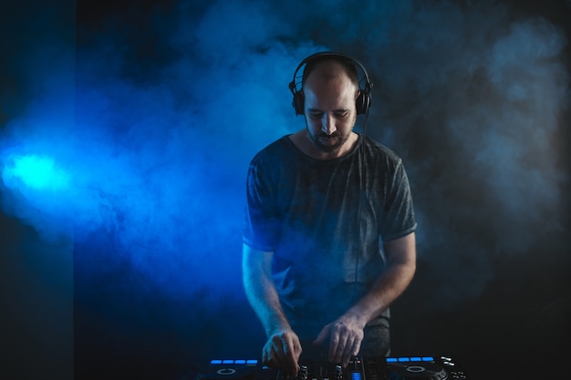 Free photo male dj working under the blue lights and smoke in a studio against a dark