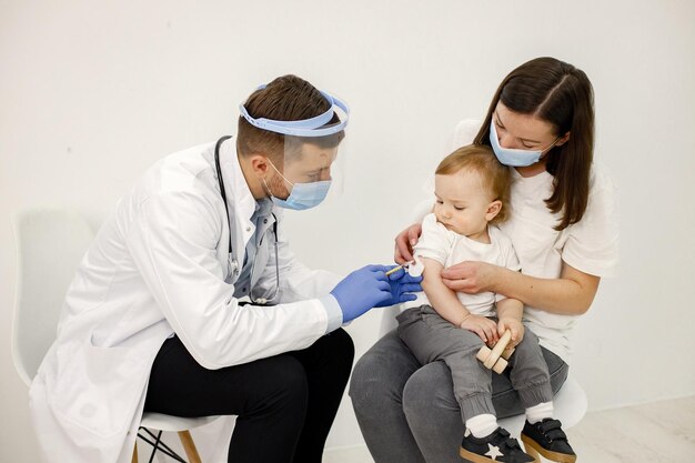 Male doctor doing a vaccination to a little boy who sitting on mother's lap