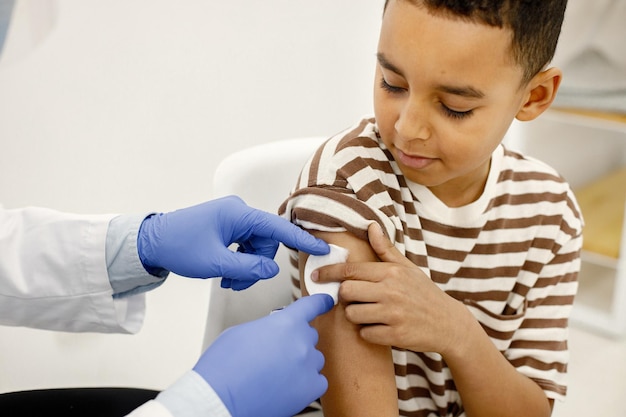 Free Photo male doctor holding a cotton on a boy's shoulders after a vaccination