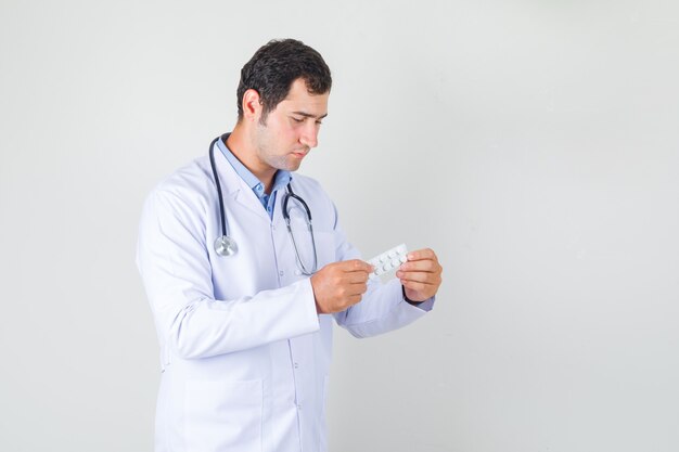 Male doctor holding pack of pills in white coat and looking serious