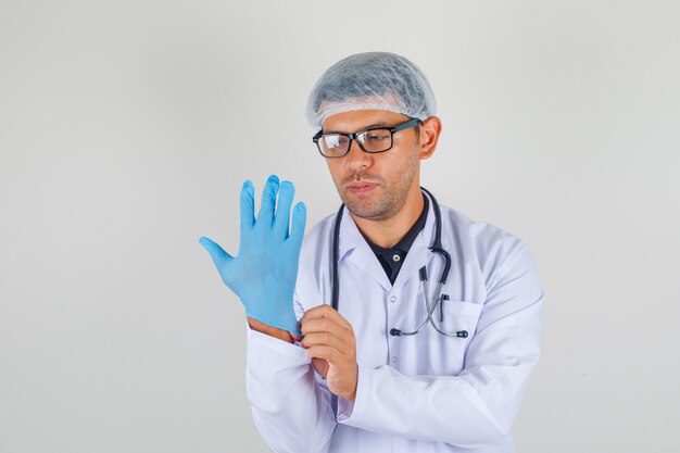 Male doctor putting on glove in medical white robe