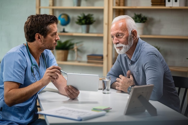 Free photo male doctor using touchpad and explaining medical test results to his senior patient during medical appointment