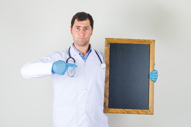 Male doctor in white coat, gloves pointing finger at blackboard and looking serious