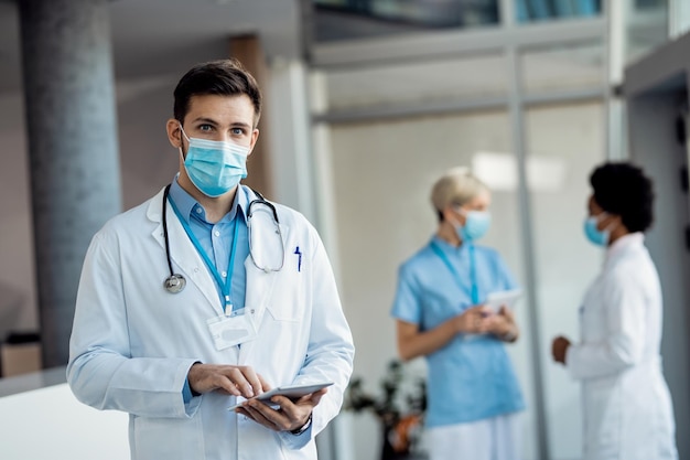 Male doctor with face mask working on digital tablet at the clinic