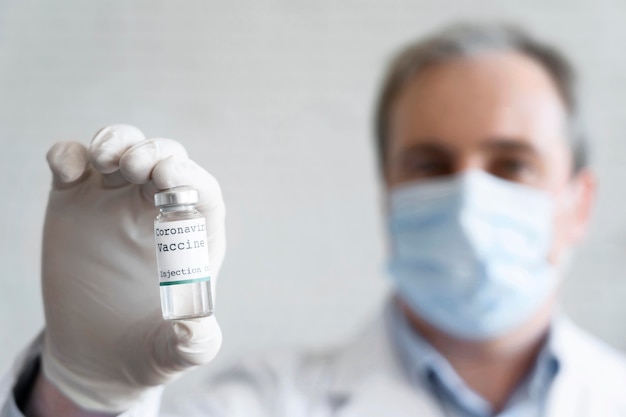 Free photo male doctor with medical mask holding vaccine