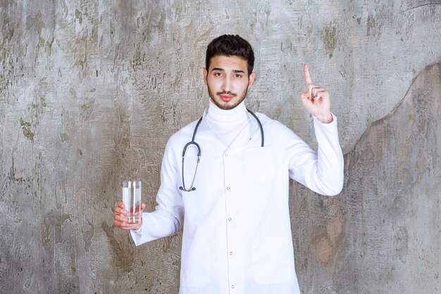 Male doctor with stethoscope holding a glass of pure water and thinking about something.