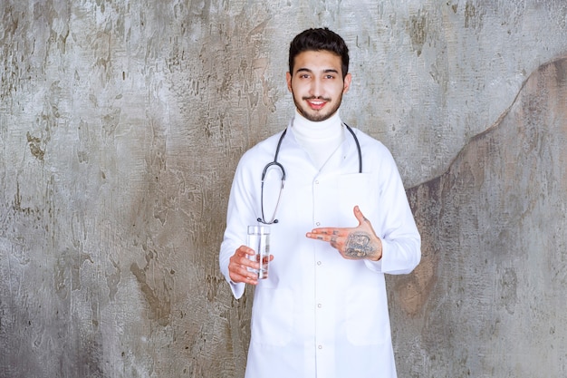 Male doctor with stethoscope holding a glass of pure water.