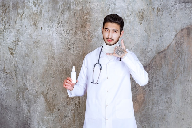 Male doctor with stethoscope holding a white hand sanitizer bottle and asking for a call