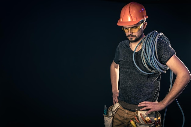 Male electrician with electric cable on a black background copy space