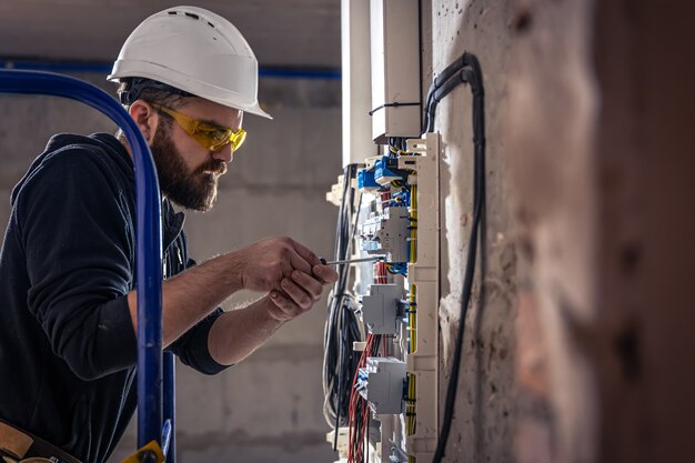 A male electrician works in a switchboard with an electrical connecting cable