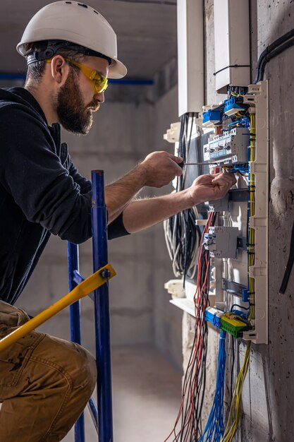 A male electrician works in a switchboard with an electrical connecting cable