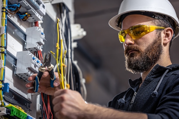 A male electrician works in a switchboard with an electrical connecting cable.