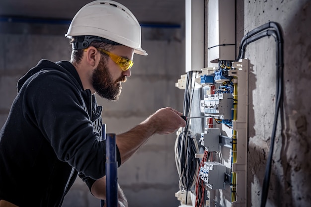 A male electrician works in a switchboard with an electrical connecting cable.