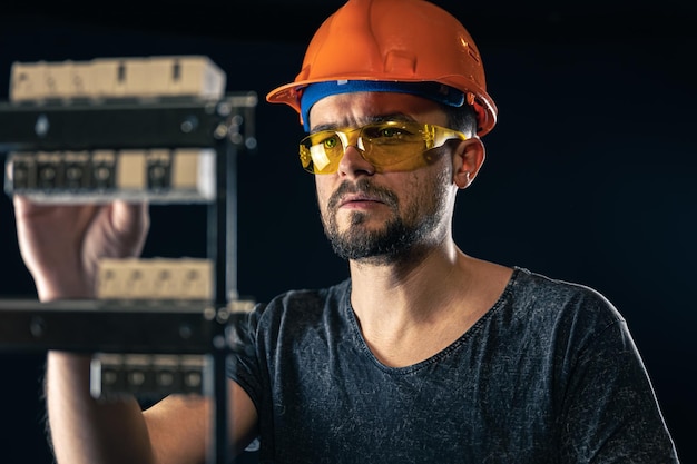 A male electrician works in a switchboard with an electrical connecting cable