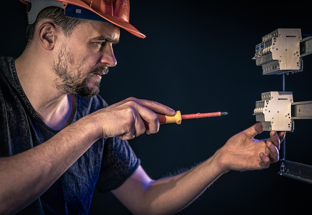 A male electrician works in a switchboard with an electrical connecting cable