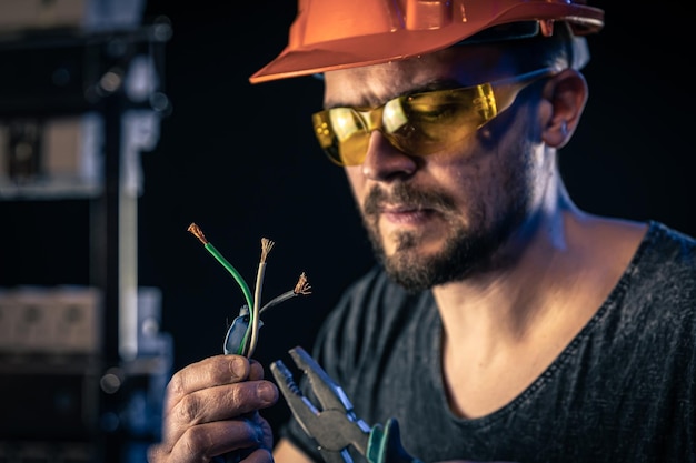 A male electrician works in a switchboard with an electrical connecting cable