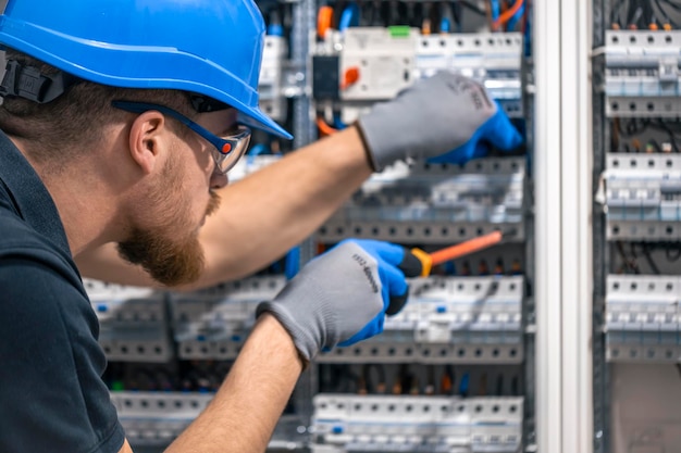 A male electrician works in a switchboard with an electrical connecting cable