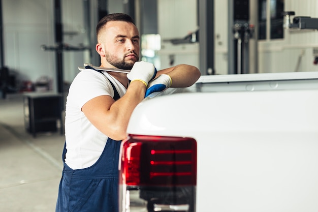 Male employee leaning on car and holding wrench