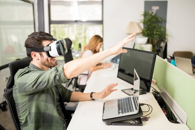 Male engineer using virtual reality glasses in office with coworker in background