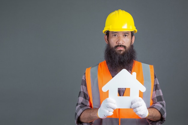 A male engineer wearing a yellow safety helmet holding a white house symbol on a gray .