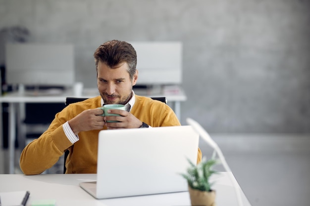 Free Photo male entrepreneur having a cup of coffee while using laptop in the office