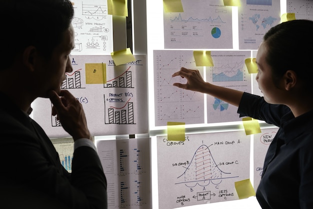 Free Photo male and female colleagues standing by window and looking at business graphs on it