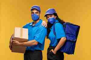 Free photo male and female deliverers with medical masks holding cardboard box and backpack