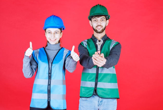 Free photo male and female engineers with helmet holding a metallic wrench and showing positive hand sign.