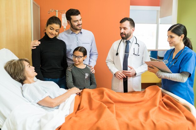 Male and female healthcare workers explaining disease to senior patient with family at hospital