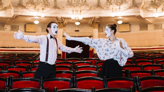 Male and female mime artist standing among chair rehearsing in auditorium