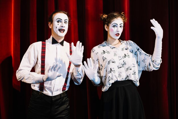 Male and female mime artist standing in front of red curtain showing hand gesture