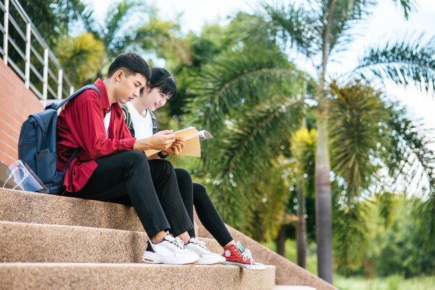 Male and female students sitting and reading books on the stairs.