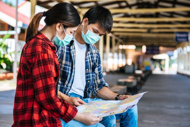 Male and female tourists look at the map beside the railway.